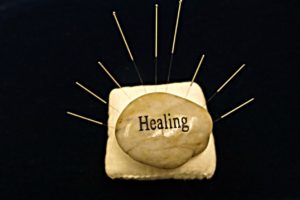 Healing stone on cushion with acupuncture needles